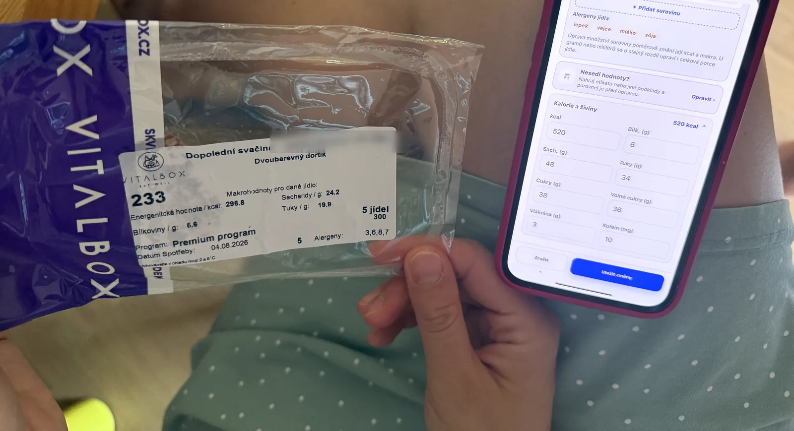 Ruka drží sáček VitalBoxu se štítkem svačiny, vedle telefon s opravou hodnot jídla v aplikaci